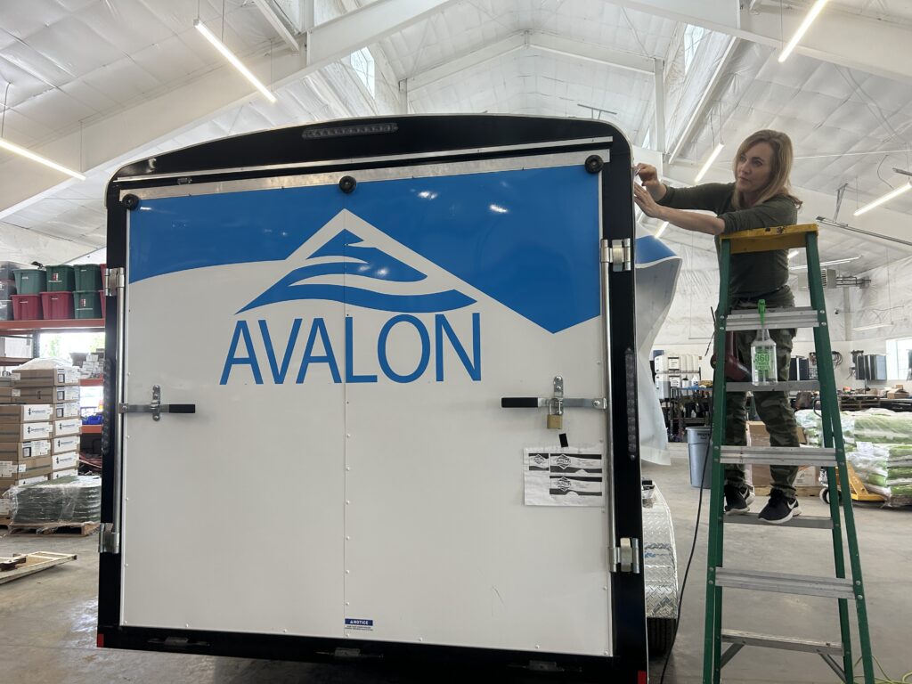 Owner of See Me Signs, Jennifer Ralphs, applies vehicles graphics to Avalon Landscaping trailers.